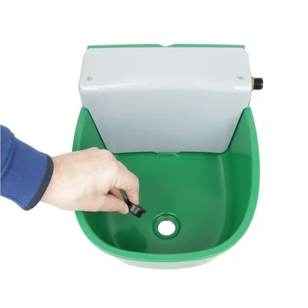 Nahaufnahme einer Hand mit blauem Ärmel, die einen kleinen schwarzen Knopf in einem grünen Kunststoffbecken betätigt; in der Mitte ist eine Abflussöffnung sichtbar, darüber sitzt ein weisser Kasten.