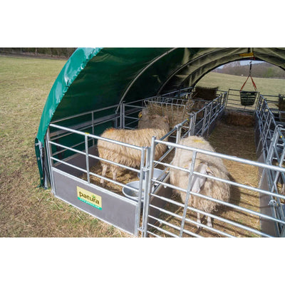 Mobiles Schafgehege aus Metallrahmen unter grünem Zeltdach; zwei wollige Schafe stehen auf Heu, Tränke und Futterrinnen im Hintergrund.