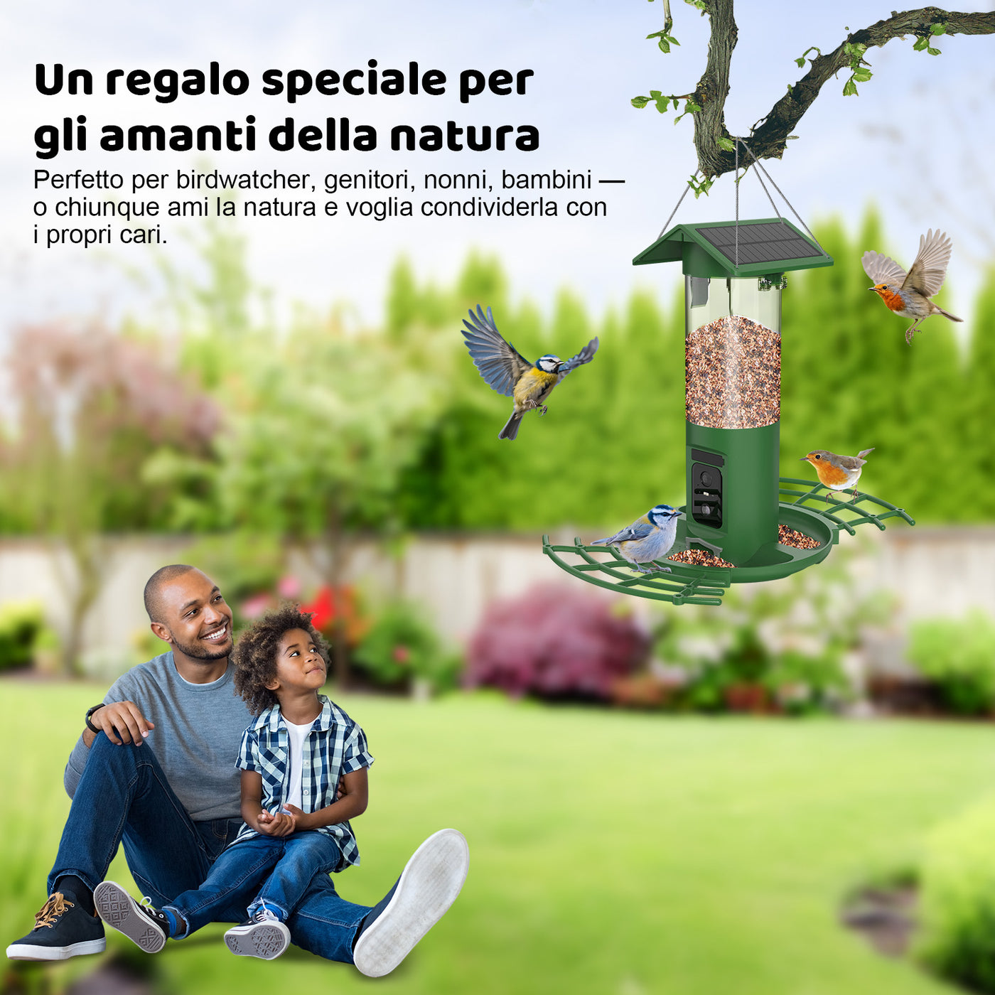 Grüner Vogelfutterspender hängt an einem Ast im Garten; mehrere Vögel fliegen um ihn, während Vater und Sohn lächelnd auf dem Rasen sitzen.