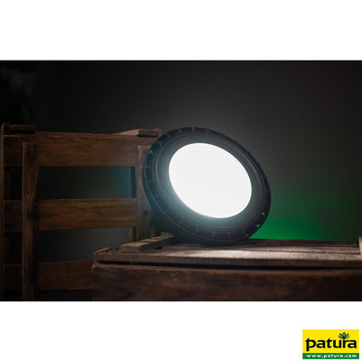 Runder LED-Scheinwerfer auf einer Holzpalette in dunkler Studioumgebung; grüne Hintergrundbeleuchtung sichtbar, Patura-Logo unten rechts.