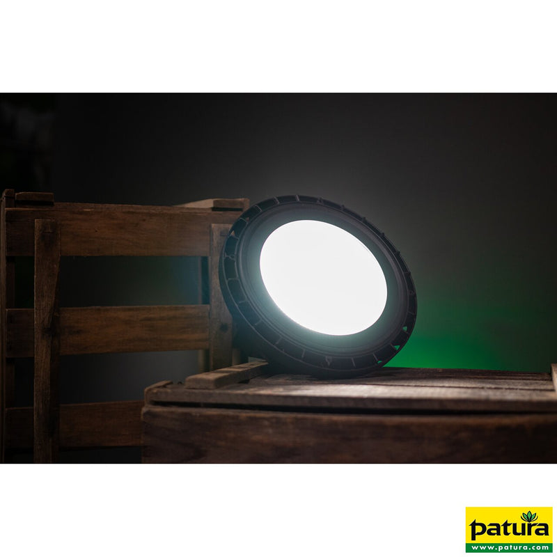 Runder LED-Scheinwerfer auf einer Holzpalette in dunkler Studioumgebung; grüne Hintergrundbeleuchtung sichtbar, Patura-Logo unten rechts.