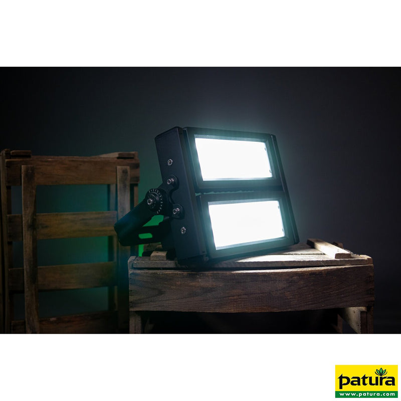 LED-Flutlicht mit zwei beleuchteten Panels, auf einer Holzkiste vor dunklem Hintergrund platziert; Patura-Logo unten rechts.