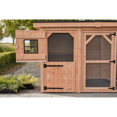 Holz-Hühnerstall im Garten mit Drahtgitterfenstern und Holztüren; kleines Fenster links, zentrale Drahtgitterfront und Tür rechts, davor Pflanzen und Kiesweg.