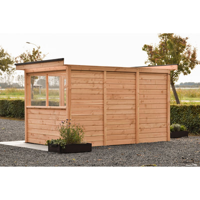 Holz-Gartenhaus aus naturbelassenem Holz mit Flachdach und Fensterfront mit Drahtgitter; vor dem Gebäude schwarzer Pflanzkübel mit lilafarbenen Blumen, Kiesboden, Hecke und Bäume im Hintergrund.