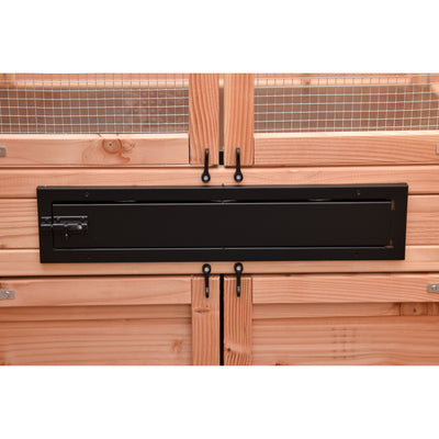 Holzverkleidung mit Drahtgitter im Hintergrund; eine lange schwarze Metalltür/Schlitzabdeckung mit Schlossmechanismus links; zwei schwarze Haken darunter; horizontale Holzplankenfassade.