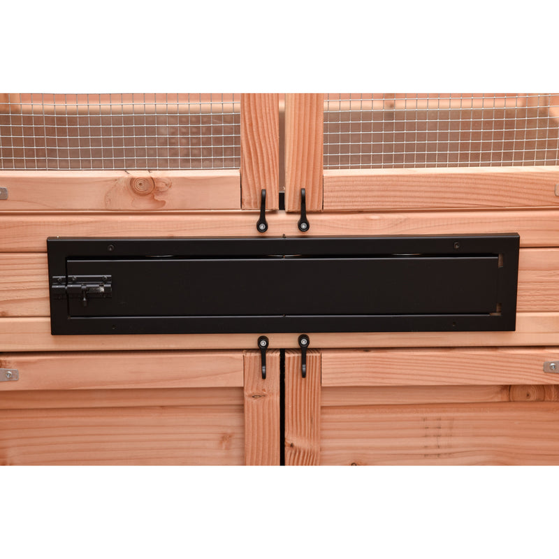 Holzverkleidung mit Drahtgitter im Hintergrund; eine lange schwarze Metalltür/Schlitzabdeckung mit Schlossmechanismus links; zwei schwarze Haken darunter; horizontale Holzplankenfassade.