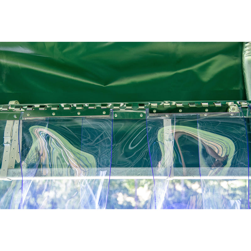 Detailansicht einer grünen Planenstruktur mit transparenten Kunststofffenstern, Metallleisten und Schraubverbindungen; reflektierende Oberflächen und draussen sichtbare Bäume.