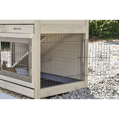 Holz-Hundezwinger im Aussenbereich mit Drahtgittertüren; linke Kammer mit Hund hinter dem Gitter, rechte Kammertür geöffnet; Kiesboden und Garten im Hintergrund.