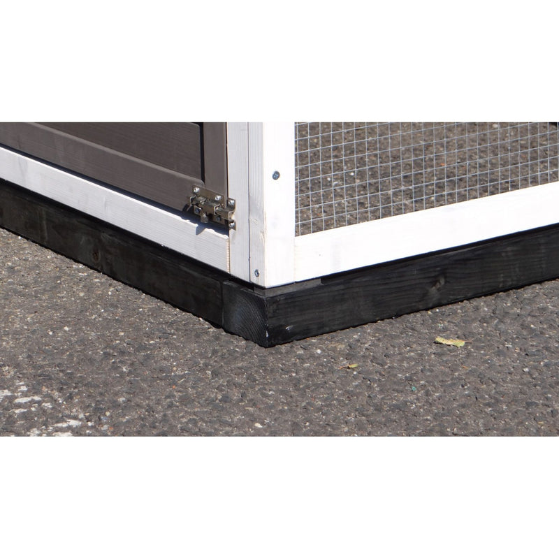 Eckansicht eines Kleintiergeheges: weisser Holzrahmen mit Drahtgitterseite, Türscharnier am unteren Rahmen, schwarzer Sockel auf Asphalt.