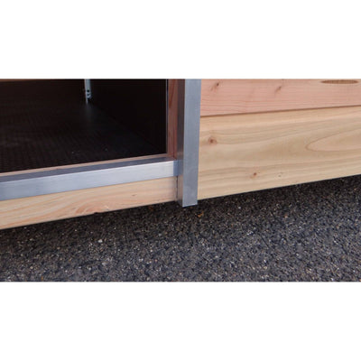 Nahaufnahme der Türöffnung eines Holzhauses: silberner Metallrahmen an der Türschwelle, offener Eingang, helle Holzverkleidung und dunkler Innenraum, asphaltierter Boden davor