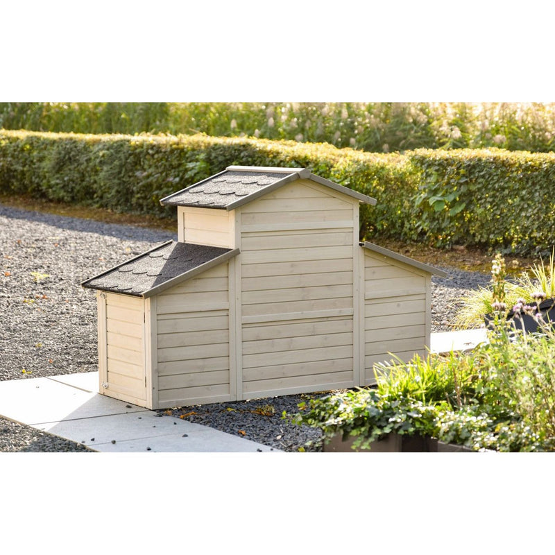 Gartenhaus aus Holz mit drei verbundenen Sektionen und grauen Schindeldächern, steht auf Kiesweg im Garten neben einer grünen Hecke.