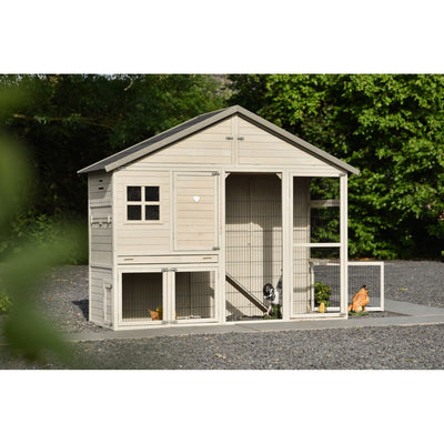 Beigefarbener Holz-Hühnerstall mit Drahtgehege und Freilauf, mehrere Hühner im Aussenbereich, Kiesweg davor und grüne Bäume im Hintergrund.