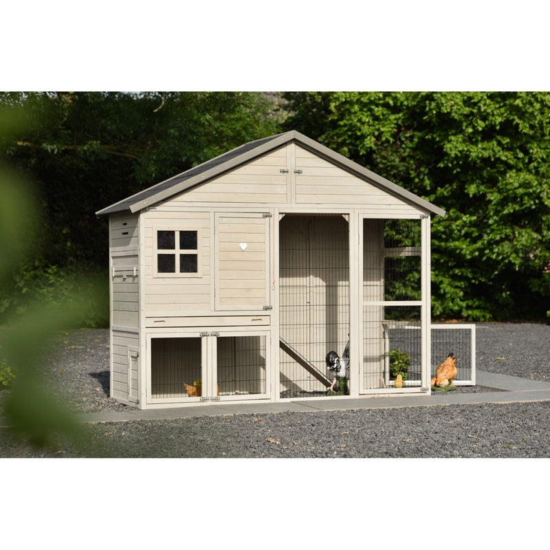 Beigefarbener Holz-Hühnerstall mit Drahtgehege und Freilauf, mehrere Hühner im Aussenbereich, Kiesweg davor und grüne Bäume im Hintergrund.