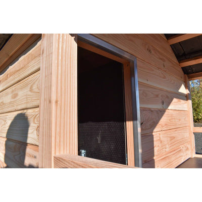 Aussenansicht einer Holzhütte mit offener Tür und Metallrahmen; horizontale Holzplankenfassade, Schatten einer Person im Vordergrund.