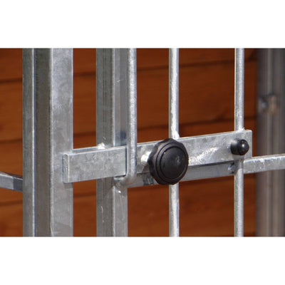 Nahaufnahme eines verzinkten Metallgitters mit Verriegelungsstange und schwarzer runder Verschlusskappe vor holzfarbenem Hintergrund.