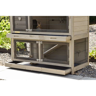 Mehrstöckiger Kaninchenstall aus Holz mit Drahtgitterfronten, zwei Ebenen, Rampe und herausziehbarem Boden, steht im Garten auf Kies.
