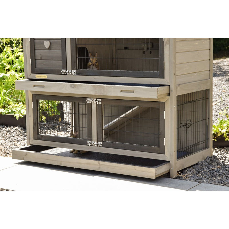 Mehrstöckiger Kaninchenstall aus Holz mit Drahtgitterfronten, zwei Ebenen, Rampe und herausziehbarem Boden, steht im Garten auf Kies.