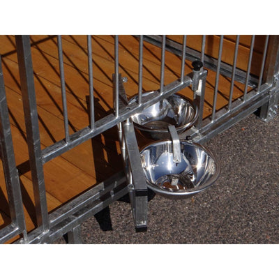 Zwei glänzende Edelstahl-Hundenäpfe hängen an einem Metallgitterzaun neben einer Holzterrasse.