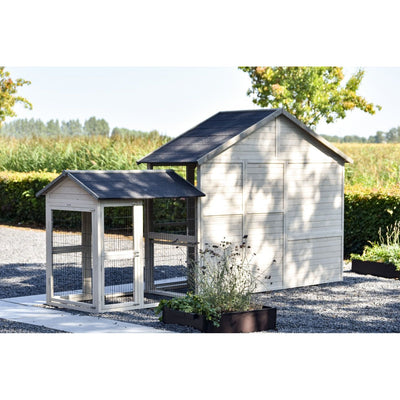 Kleiner Hühnerstall mit Drahtgehege neben einem grösseren Holzhäuschen im Garten, Kiesboden, Pflanzkübel vorne, Hecken und Felder im Hintergrund.