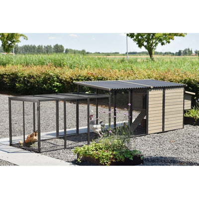 Hühnerstall mit Drahtgehege und angeschlossenem Holzschuppen auf Kies, Hühner und Küken im Gehege; umliegender Garten mit Pflanzen und Feldern im Hintergrund.