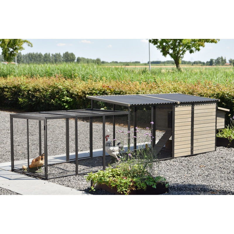 Hühnerstall mit Drahtgehege und angeschlossenem Holzschuppen auf Kies, Hühner und Küken im Gehege; umliegender Garten mit Pflanzen und Feldern im Hintergrund.