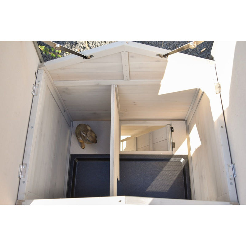 Von oben sichtbarer heller Holzkasten mit getrennter Innenaufteilung; in der linken Kammer liegt ein kleines braunes Säugetier, Deckel offen.