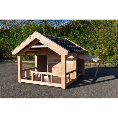 Holzspielhaus mit Veranda im Garten, dunklem Schrägdach, auf Asphaltfläche.