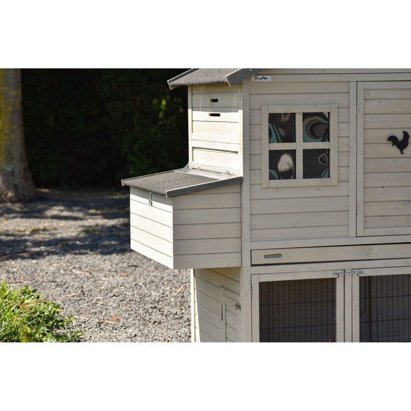 Weisser Holz-Hühnerstall mit Fenster, kleinem Seitenteil und Drahtgehege unten, steht auf Kies, schwarze Hahnensilhouette an der Aussenwand.