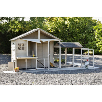 Holz-Hühnerstall mit Freilaufgehege aus Drahtgitter, Kiesboden, mehrere Hühner im Auslauf vor grünem Hintergrund.
