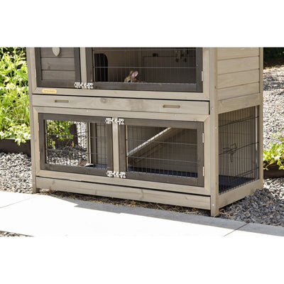 Zweistöckiger Hasenstall aus Holz mit Metallgittertüren; Kaninchen in den Käfigen, Aussenbereich auf Kiesboden.