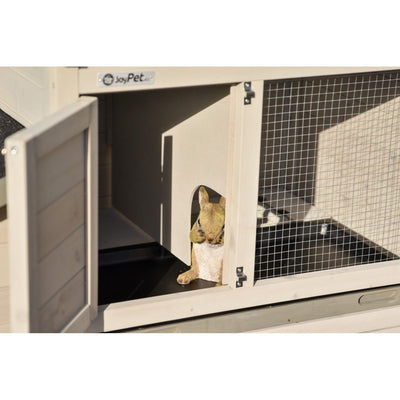 Kleines braunes Kaninchen schaut aus dem offenen Eingang eines Holz-Käfighauses mit Drahtgitter-Seite im Aussenbereich.