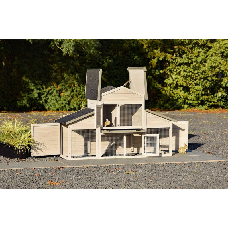 Mehrstöckiger Holz-Kaninchenstall mit Drahtgitter, draussen auf Kiesboden; ein Kaninchen schaut aus dem oberen Gehege, ein zweites sitzt am Stallrand.