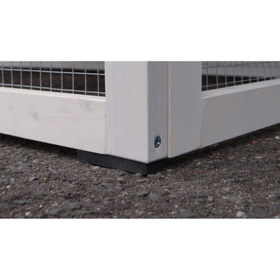 Unteres Eckstück eines weissen Holzrahmens mit Drahtgitter, Schraube und schwarzem Gummifuss auf grobem Kiesboden.