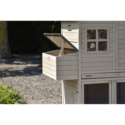 Weisser Holzhühnerstall mit seitlich herausziehbarem, offenem Nistkasten und geöffnetem Deckel; Fenster mit Rahmen und Maschendraht unten, Kiesboden im Hintergrund.