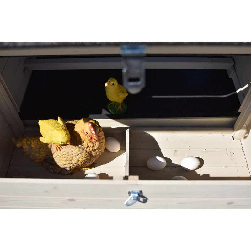 Holznestkasten mit mehreren weissen Eiern; eine grosse gelb-braune Hühnerfigur liegt im Nest, daneben kleinere gelbe Kükenfiguren bei Tageslicht.