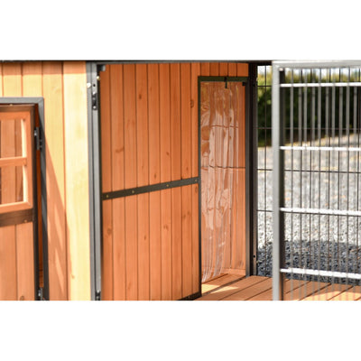 Holzstall aus vertikalen Holzbrettern mit schwarzen Metallbeschlägen, geöffnetem Türblatt und angrenzendem Metallgitterzaun im Aussenbereich.