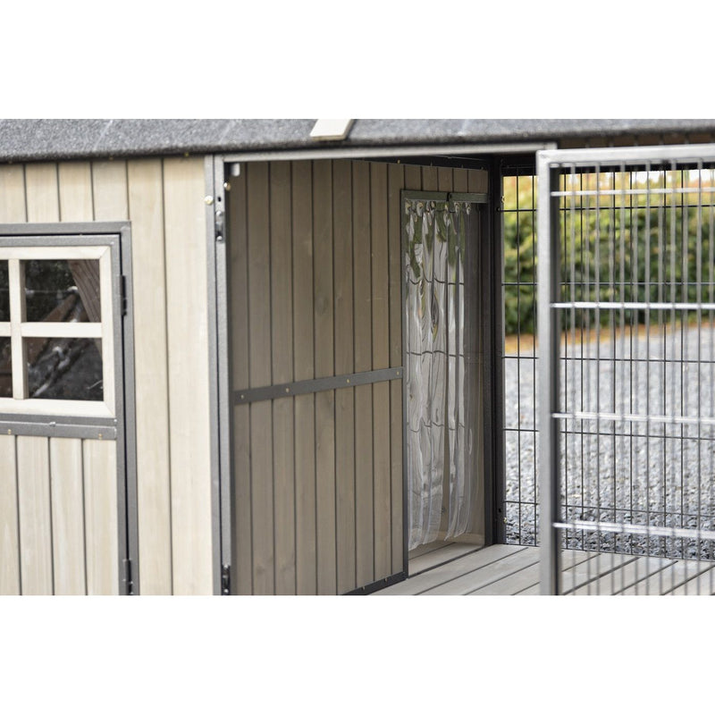 Kleiner Holzhäuschen-Hundezwinger mit offener Tür, links Fenster mit weissem Rahmen, daneben Metallgitterzaun und Kiesweg im Hintergrund.