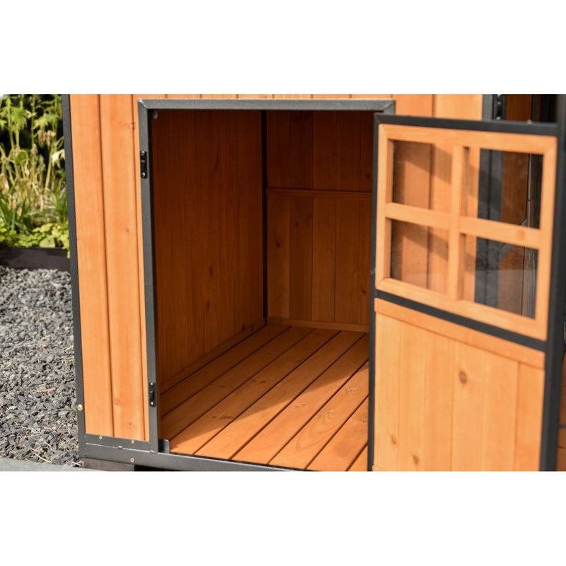 Offener Holzschuppen aus warmem Holz mit Türfenster; Innenraum aus Holzpaneelen und Holzboden sichtbar; steht auf Kies neben Gartenpflanzen.