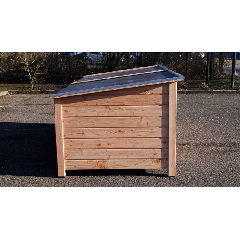 Kleiner Garten-Holzschuppen aus hellen Brettern mit schrägem Metall-Dach auf Asphalt, Hintergrund mit Bäumen.