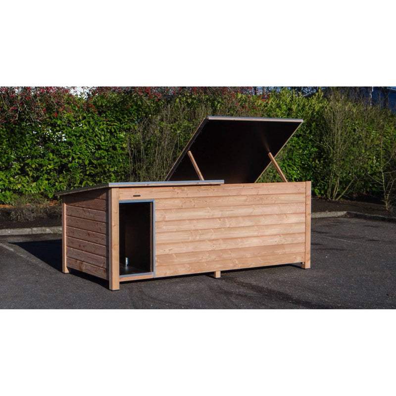 Grosses rechteckiges Holzgehäuse mit geöffnetem Deckel im Freien, auf Asphalt neben einer grünen Hecke.