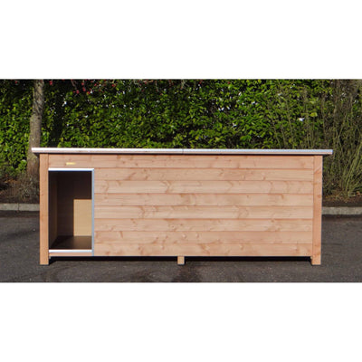 Langgestreckter Hühnerstall aus naturbelassenem Holz mit offener Tür links; horizontale Bretter, silberner Türrahmen, steht auf Asphalt vor einer dichten grünen Hecke.