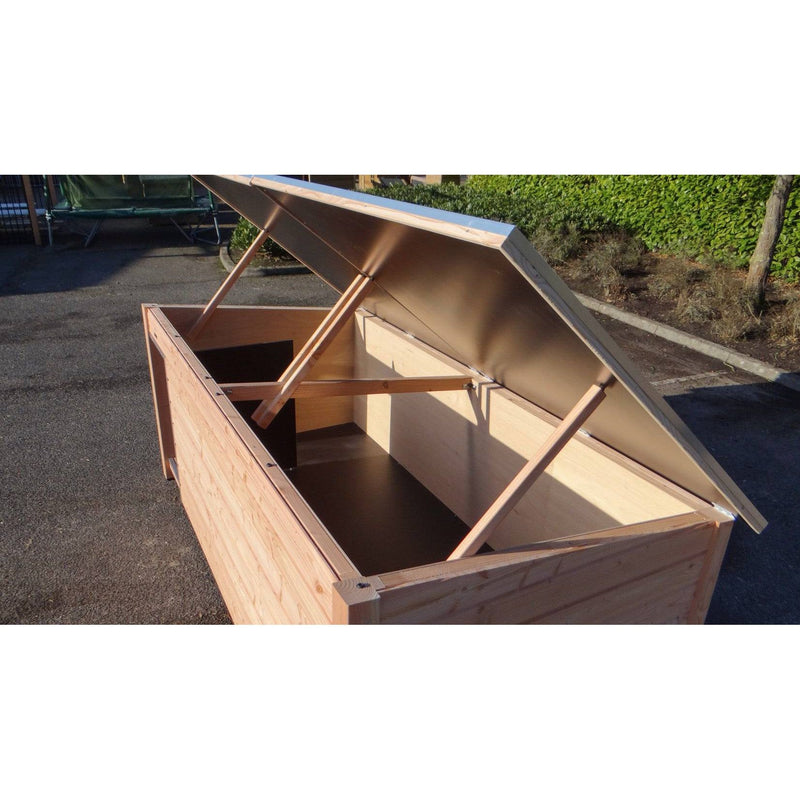 Grosse Holzkiste mit geöffnetem Deckel, von Stützstreben gehalten, Innenraum sichtbar, steht auf Asphalt im Freien.