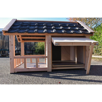 Holz-Hühnerstall mit dunklem Ziegeldach, offener Eingang und seitlichem Verschluss, steht auf Asphalt im Garten.