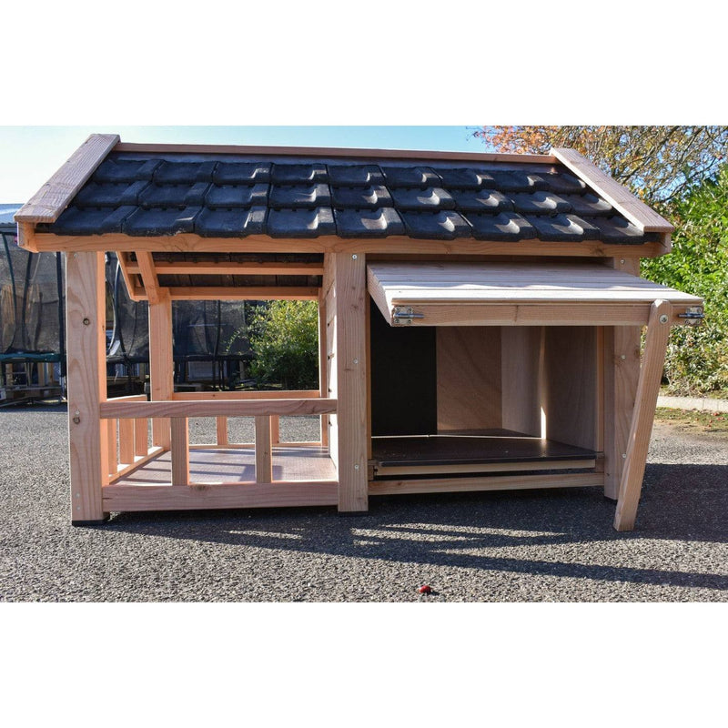 Holz-Hühnerstall mit dunklem Ziegeldach, offener Eingang und seitlichem Verschluss, steht auf Asphalt im Garten.