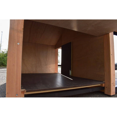 Innenraum eines offenen Holzunterstands mit dunklem rutschfestem Bodenbelag, offener Tür und Blick nach aussen auf Kies.