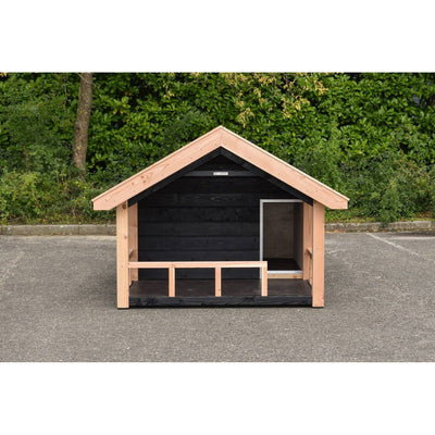 Kleines Garten-Holzhaus mit Satteldach und offener Front, naturbelassene Holzbalken, dunkle Innenwände, steht auf Asphalt vor grünem Buschwerk.