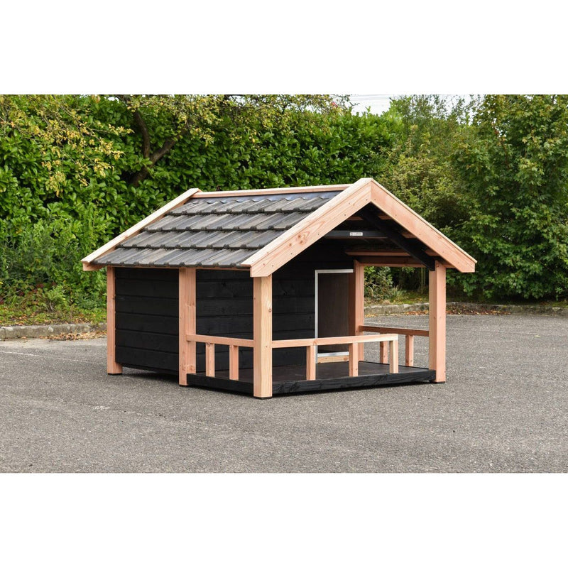 Holz-Spielhaus für Kinder mit schwarzer Wand, hellen Holzbalkenrahmen, offener Veranda und Satteldach mit grauen Dachziegeln, stehendes auf Asphalt vor grüner Hecke.