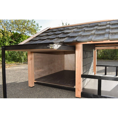 Gartenunterstand aus Holz mit schwarzer Metallkonstruktion, offener Vorderseite, Holzboden, Dach aus dunkelgrauen Tonziegeln, steht auf Asphalt neben Bäumen.