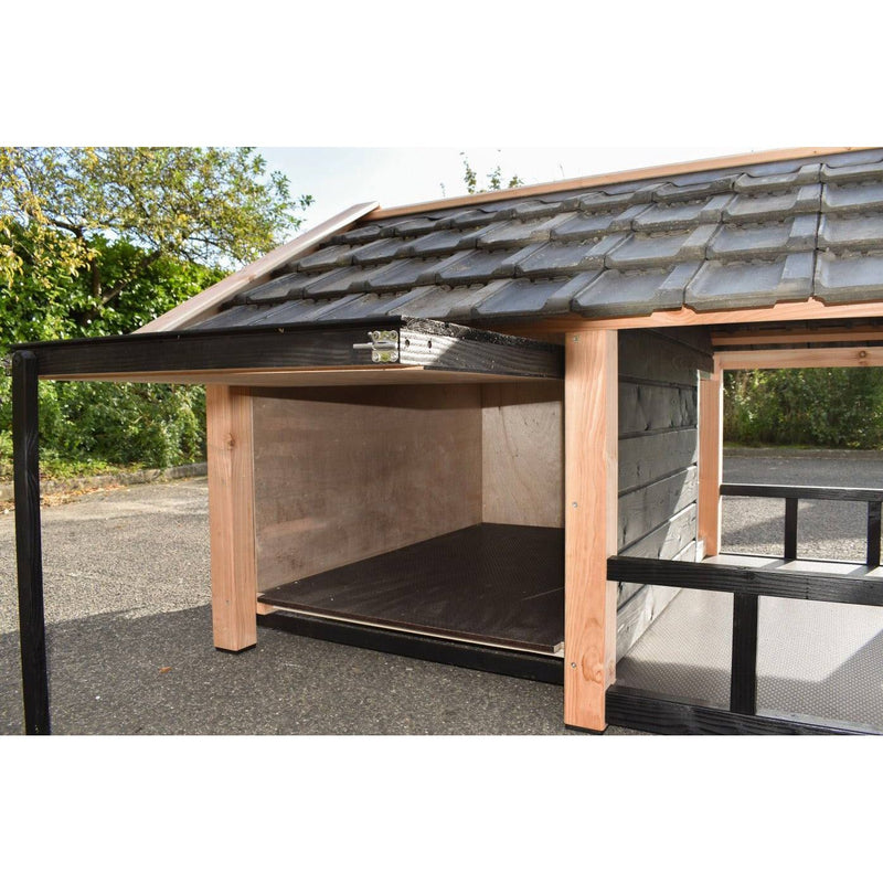 Gartenunterstand aus Holz mit schwarzer Metallkonstruktion, offener Vorderseite, Holzboden, Dach aus dunkelgrauen Tonziegeln, steht auf Asphalt neben Bäumen.