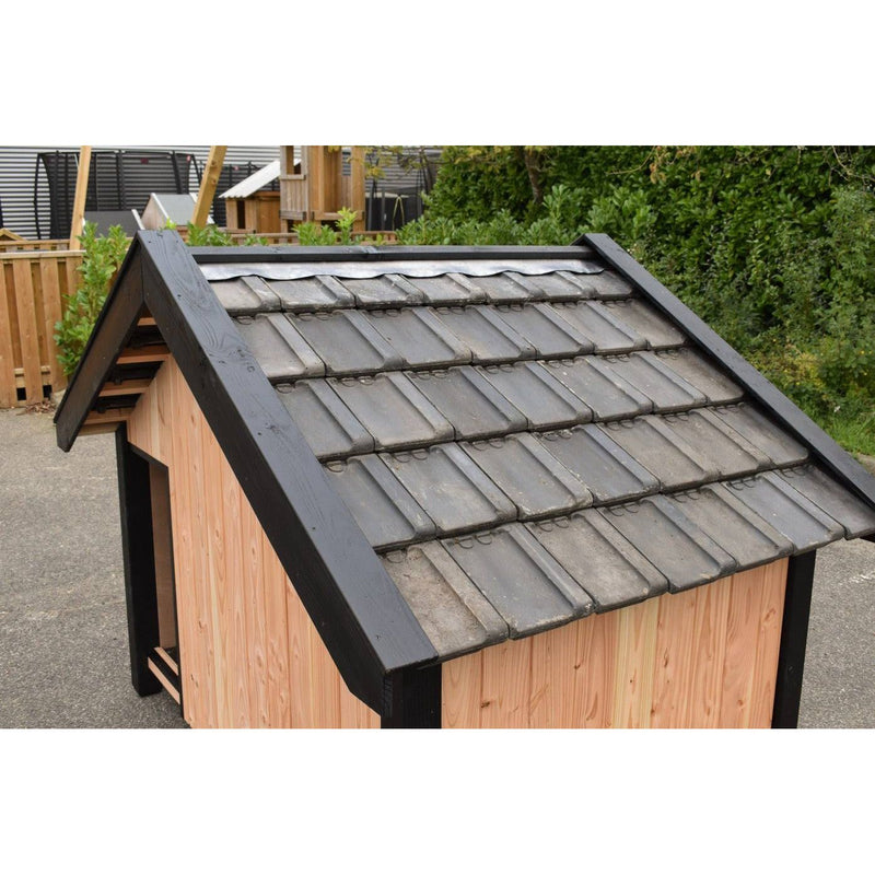 Hundehütte aus Holz mit schwarzem Dach und grauen Dachziegeln im Garten.